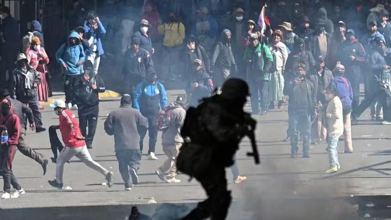 Um policial corre em frente a manifestantes durante uma marcha que pede a renúncia do presidente boliviano Rodrigo Paz , em meio ao agravamento da crise econômica e de combustíveis no país, devido à escassez de dólares americanos e à queda na produção interna de energia, em La Paz , Bolívia, 25 de maio de 2026.