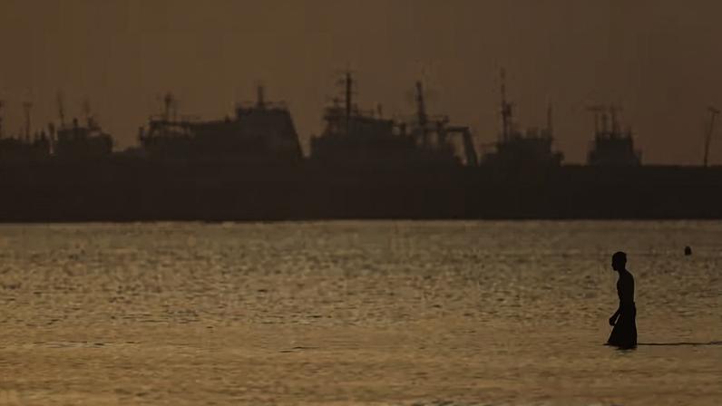 Um homem iraniano está na água na praia, com embarcações visíveis no Estreito de Ormuz , perto da praia de Bandar Abbas, Irã, 1º de junho de 2026.