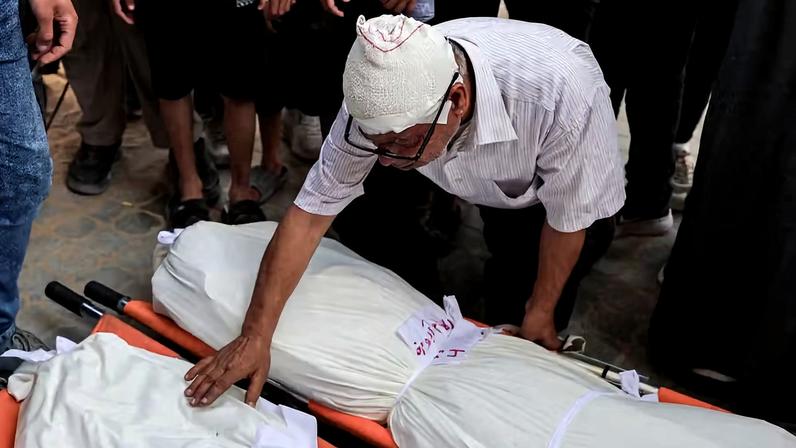 O palestino Naaman Abu Maraq, ferido em um ataque israelense a um apartamento, debruça-se sobre os corpos de familiares mortos no mesmo ataque, durante o funeral na Cidade de Gaza , em 4 de junho de 2026