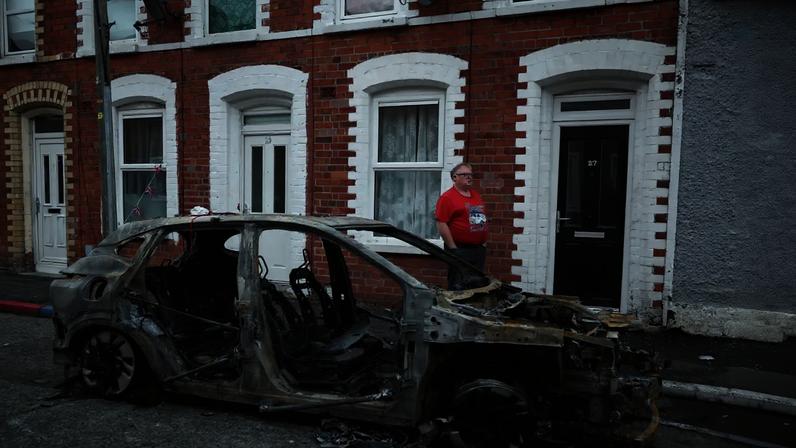 Morador ao lado de carro queimado após protestos anti-imigrantes em Belfast 10 de junho de 2026 REUTERS/Isabel Infantes