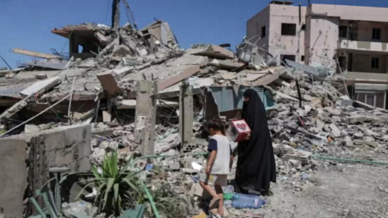Uma mulher que retorna à sua aldeia após ser deslocada pela guerra segura uma caixa resgatada da casa de sua vizinha, destruída por um ataque israelense, em Qlaileh, distrito de Tiro, sul do Líbano , 19 de junho de 2026