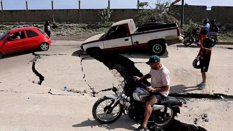 Homem sentado em uma motocicleta em uma rua danificada após os terremotos que atingiram a Venezuela