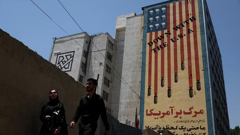 Pessoas caminham perto de um mural anti-EUA em Teerã, Irã , 28 de junho de 2026