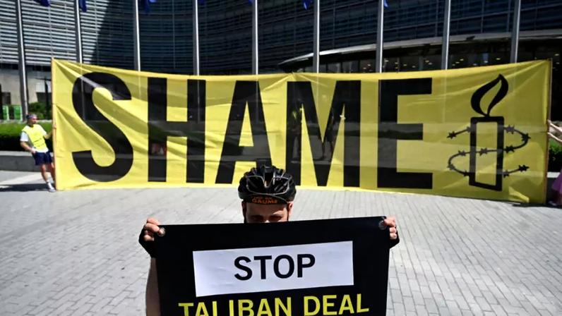 Um ativista da Anistia Internacional segura uma faixa com os dizeres "Parem com o acordo com o Talibã" em frente à sede da Comissão Europeia, em protesto contra uma reunião com uma delegação do Talibã em Bruxelas, em 23 de junho de 2026.