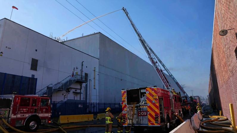 Fire trucks spraying water over a building with smoke billowing overhead.