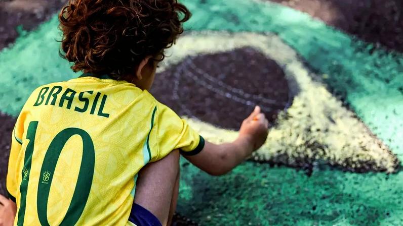 Criança pinta a bandeira do Brasil na rua, parte da decoração para Copa do Mundo