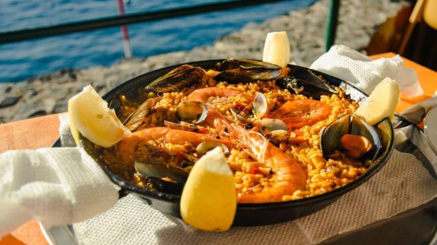 Panela preta servida com o prato paella em uma mesa de frente para o mar.