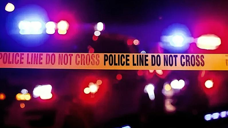 Getty Images Purple and pink flashing police lights are in rack focus in the distance with yellow police tape that says police line do not cross on it in the foreground.