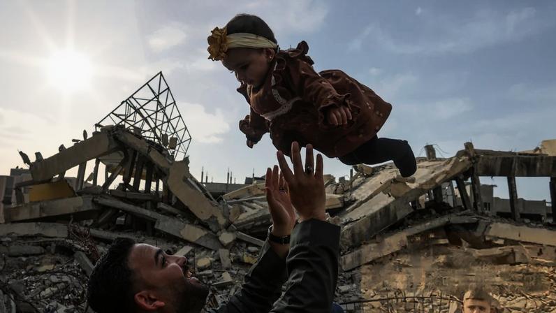 A man plays with a baby as Palestinian children look on amid the rubble in Khan Younis, Gaza, in March.