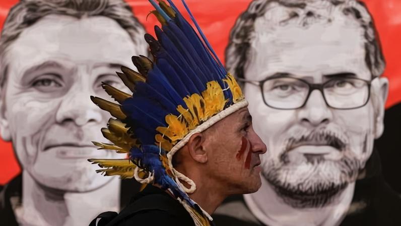 An Indigenous demonstrator in Brasília, Brazil, walks past a poster of the British journalist Dom Phillips and Bruno Pereira, who worked with an Indigenous organisation, after the men went missing in the Amazon in 2022.
