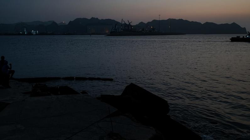 A man exercises across the waters off Oman where oil tankers, carriers, vessels and Omani fisher boats sit anchored around Qaboos Port in Muscat, Oman.