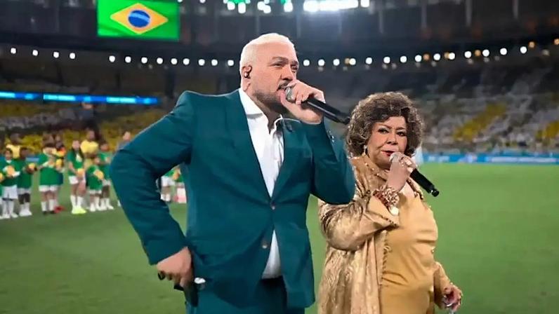 Belo e Alcione cantam o hino nacional brasileiro durante jogo do Brasil no Maracanã.