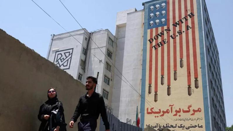 Pessoas caminham perto de um mural anti-EUA em Teerã, no Irã, em 28 de junho de 2026.