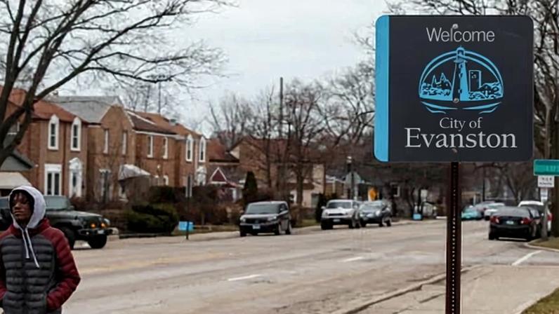A young man walks in a residential neighborhood past a sing that says 'Welcome. City of Evanston'.