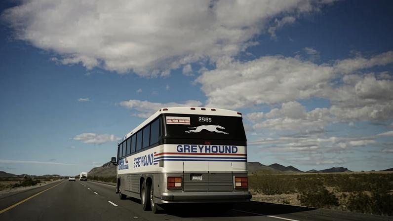 a bus drives down a highway with a blue sky and clouds overhead