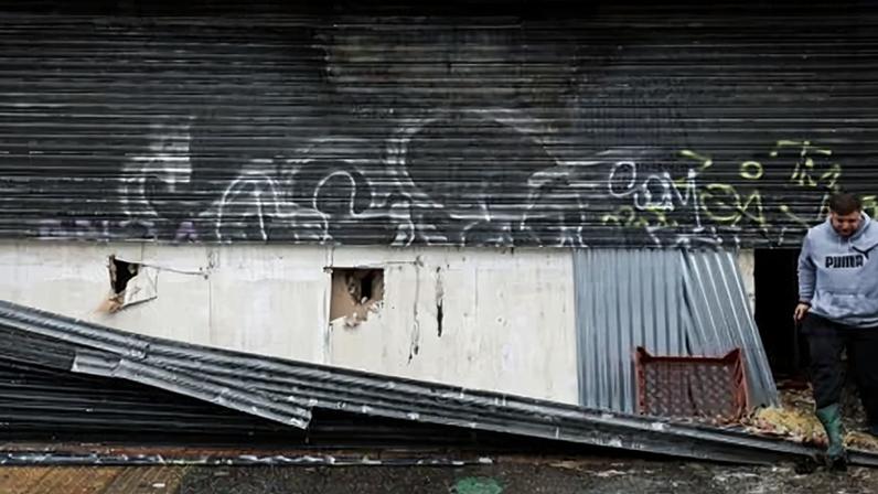 A man inspects the damage to a shop that rioters targeted on Wednesday night.