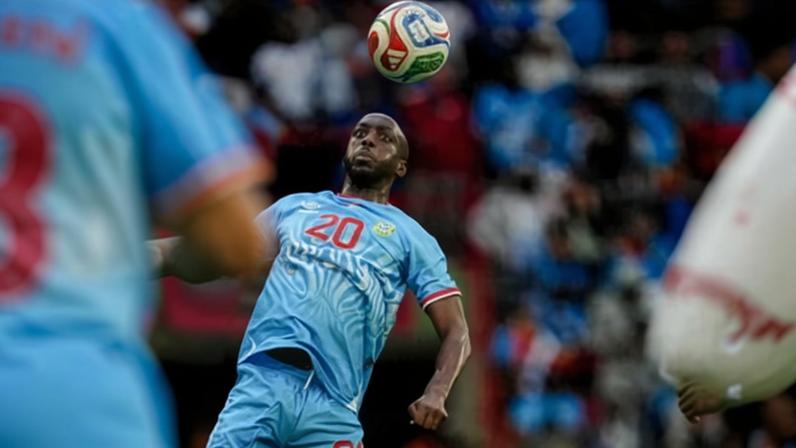 Yoane Wissa in a light blue jersey looks up at a ball in the air during a match