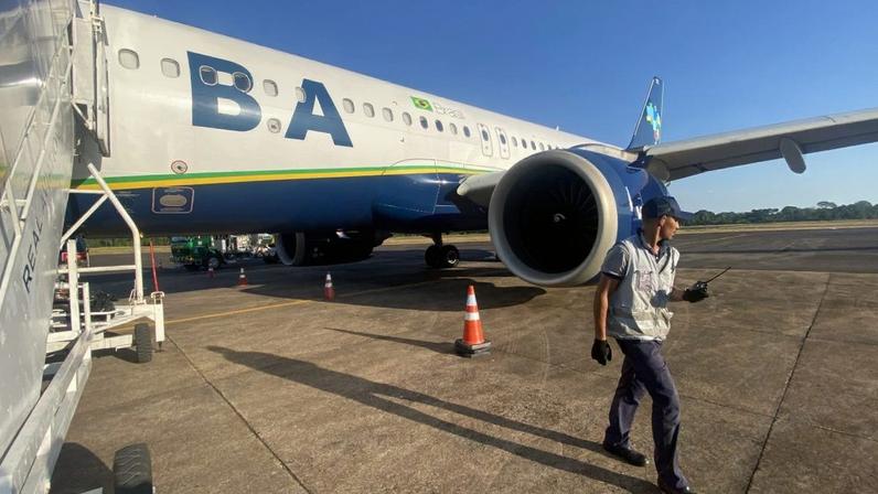 Funcionário da Azul caminha no pátio, próximo a avião da Azul com escada de embarque