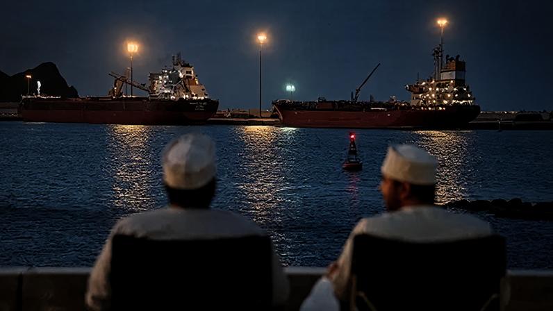 Reuters The backs of two men wearing white can be seen looking out to sea, where the Galaxy Globe bulk carrier and the Luojiashan tanker sit anchored as Iran vows to close the Strait of Hormuz, amid the U.S.-Israeli conflict with Iran, in Muscat, Oman, March 9, 2026. REUTERS/Benoit Tessier/File Photo