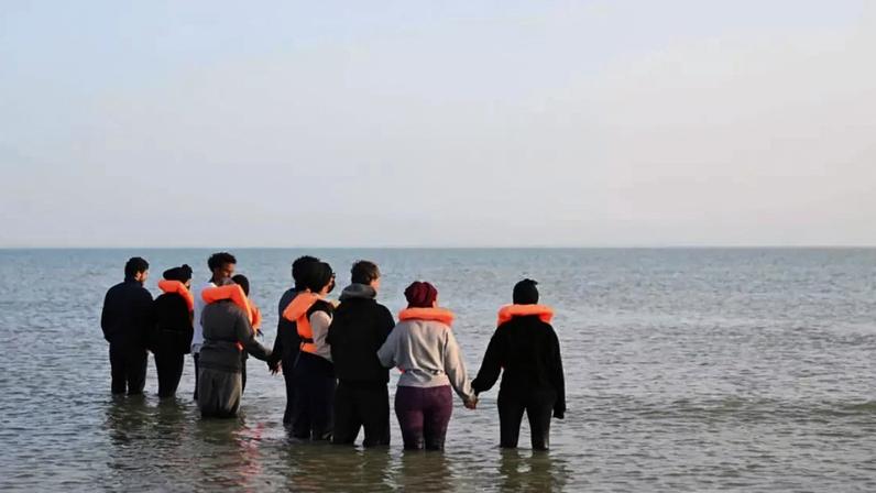 Grupo de migrantes caminham pela água para embarcar em um bote no norte da França para tentar atravessar o Canal da Mancha, em 23 de maio de 2026.