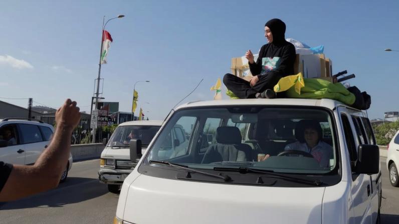 Libanesa deslocada segura cartaz do falecido líder do Hezbollah, Hassan Nasrallah, enquanto volta para casa com familiares no sul do Líbano.