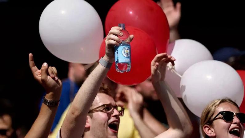 Torcedor do Arsenal segura garrafa de água personalizada com a logo do Manchester City -