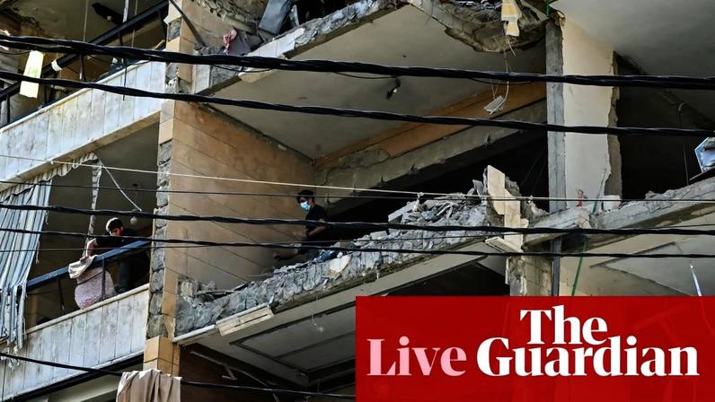 People wearing masks stand on exposed floors of a heavily damaged residential building with dangling power lines