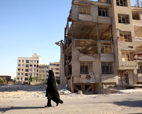 A woman walks past a destroyed building
