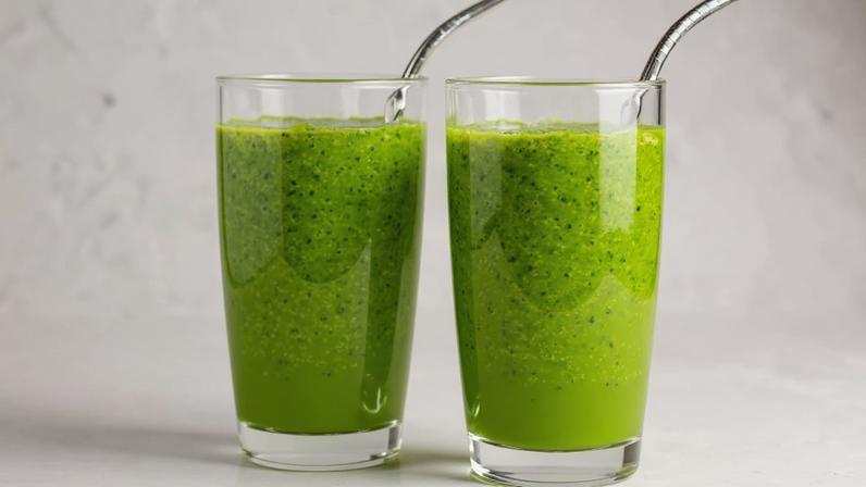 Dois copos de suco verde com canudo de aço à frente de várias folhas verdes.