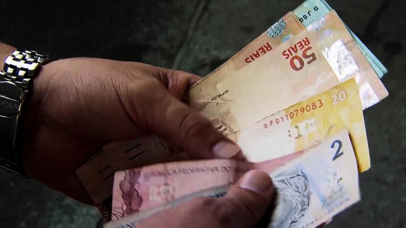 Pessoa segurando notas de real, a moeda brasileira. É possível ver cédulas de 2, 20 e 50 reais.