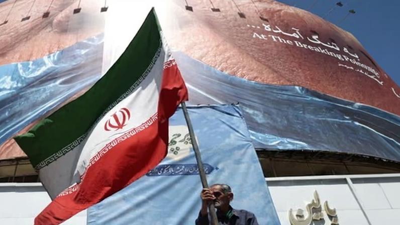 A man holds an Iranian flag near an anti-US billboard depicting Donald Trump and the strait of Hormuz, in Tehran, Iran on 30 May.