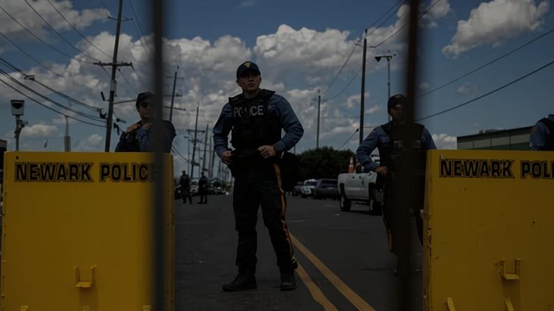 Police officers in tactical vests stand behind yellow barricades on a street with utility poles overhead