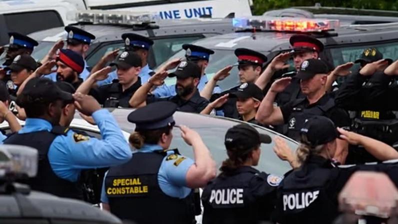 Police salute during a procession with the body of Constable Marc Pinizzotto, who was killed in the line of duty conducting a raid earlier in the day, in Toronto on 11 June 2026.