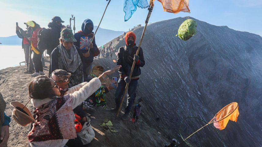 People holding colourful nets on poles gather on Mount Bromo's crater rim under clear skies