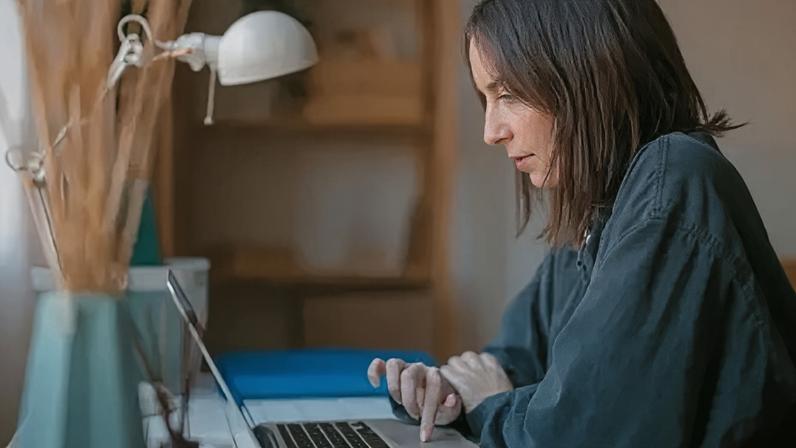 Getty Images Side view of woman in black shirt sitting at her desk while using a laptop.