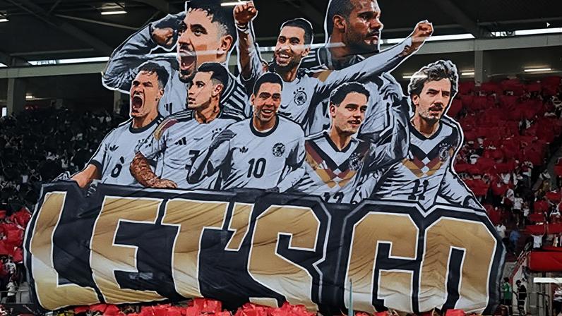 A large banner featuring German football players is held up in a stadium with red seats