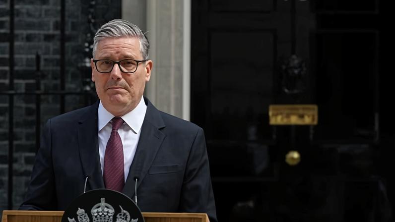 Starmer in jacket and tie behind lectern outside door of No10 looking pensive