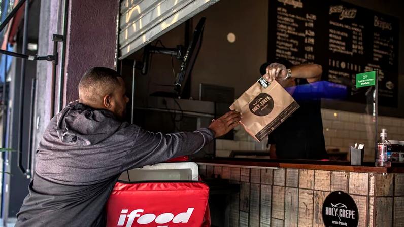 Entregador retira pedido em restaurante para entrega pelo aplicativo iFood em São Paulo