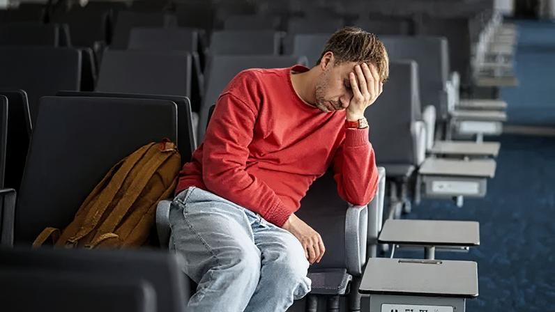 Getty Images A man in a red jumper sits with his head in his hand at a bank of airport teminal seats.