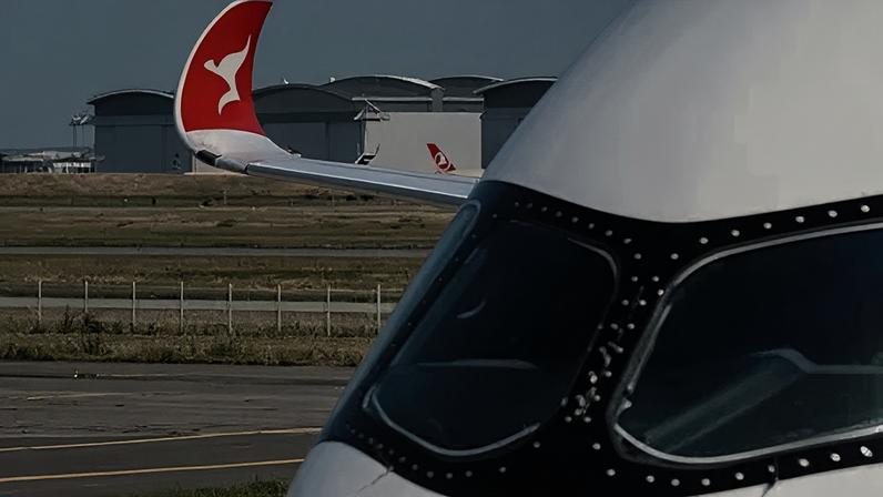 Qantas A close up of an airplane's cockpit, with the wingtip visible in the distance with the red and white kangaroo logo of Qantas.