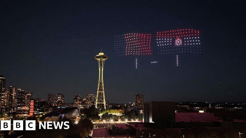 The Seattle skyline at night with drones lights showing flags and 1-1