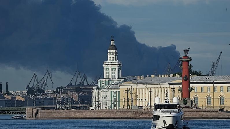 Cars near a banner for the economic forum, with black smoke rising in the distance