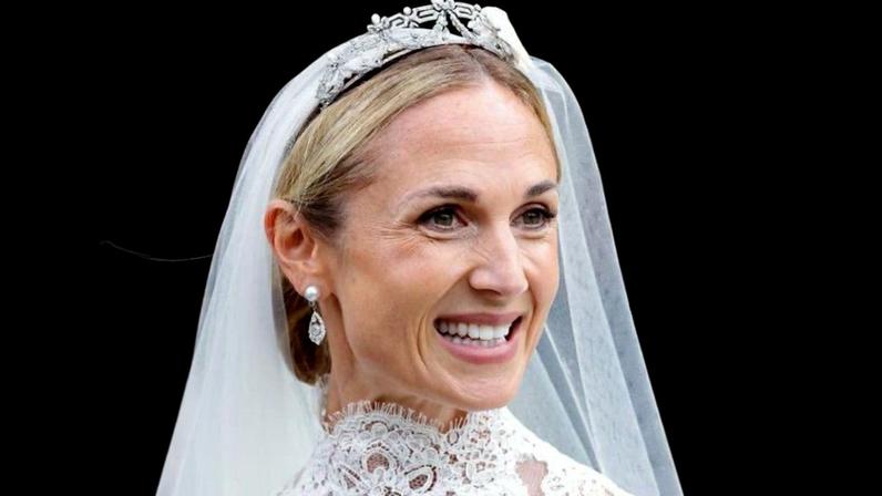 Harriet Sperling, wearing pearl earrings with a silver drop, a veil and a tiara, smiles. She's wearing a high-necked wedding dress