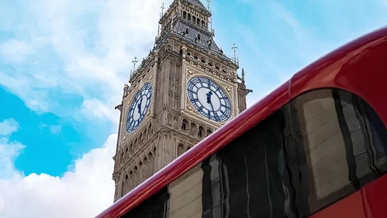 Getty Images Big Ben clock tower at the Palace of Westminster in London viewed from below, with a red double‑decker bus passing in the foreground against a blue sky with scattered clouds.