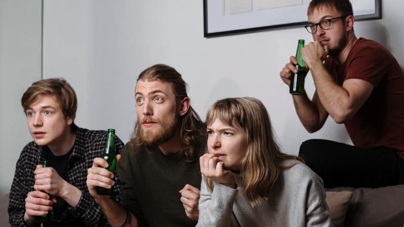 De acordo com especialistas, os filmes de terror refletem os medos de cada época. E 'The Backrooms' mostra quais são os fantasmas da Geração Z Group of friends sitting on sofa and intently watching movie together with chips and beer at home. Group of young people showing defferents emotions while watching film