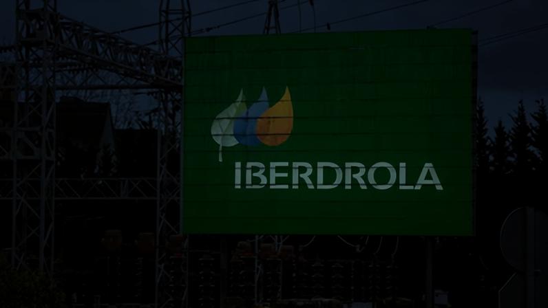 Un cartel con el logotipo de Iberdrola junto a una subestación eléctrica.