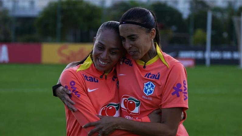 Adriana e Andressa Alves abraçadas com a camisa de treino laranja da seleção brasileira