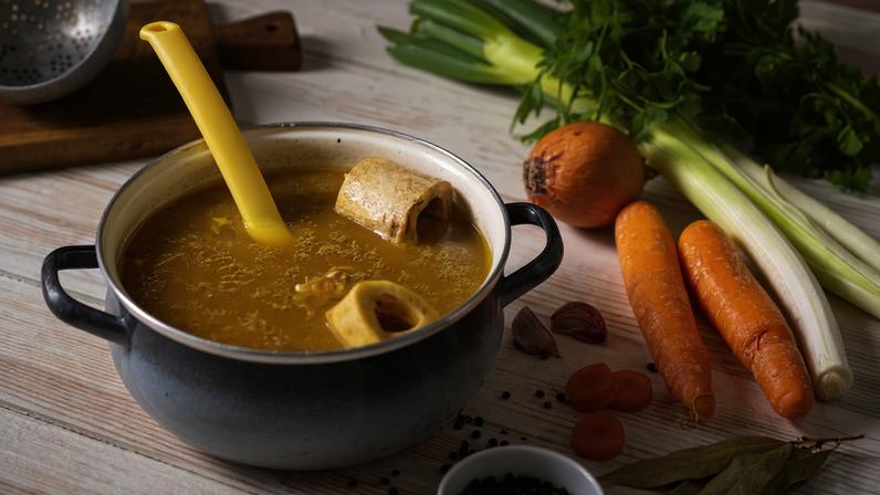 Foto colorida de panela com caldo de ossos. Ao lado, cebola, alho-poró e cebola - Metrópoles