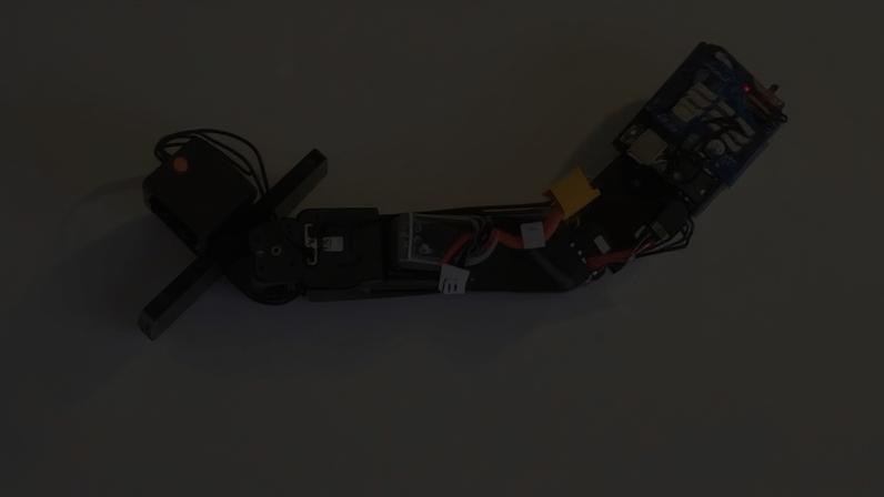 Braço robótico preto articulado com fios e circuitos expostos, sobre um fundo branco liso