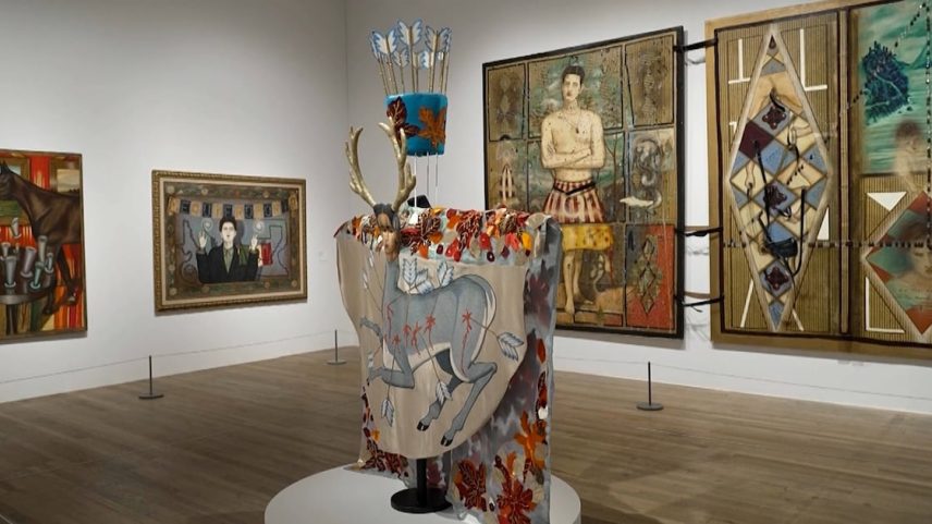 Sala de exposição com pinturas e instalação artística em destaque sobre pedestal, cercada por obras de arte nas paredes